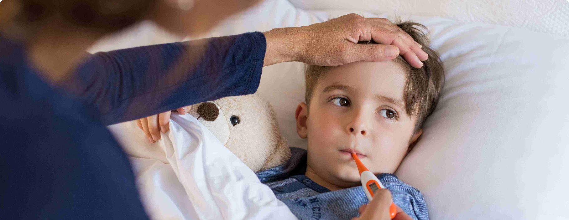 Nino con fiebre acostado en cama mientras un adulto toma su temperatura